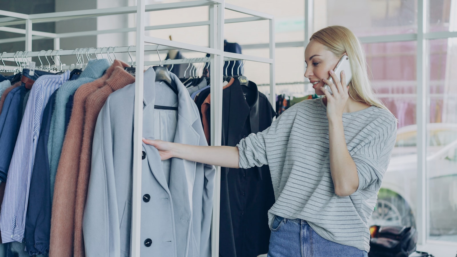 Pessoa em uma loja de roupas, ao telefone, atravessando o canal físico e o digital